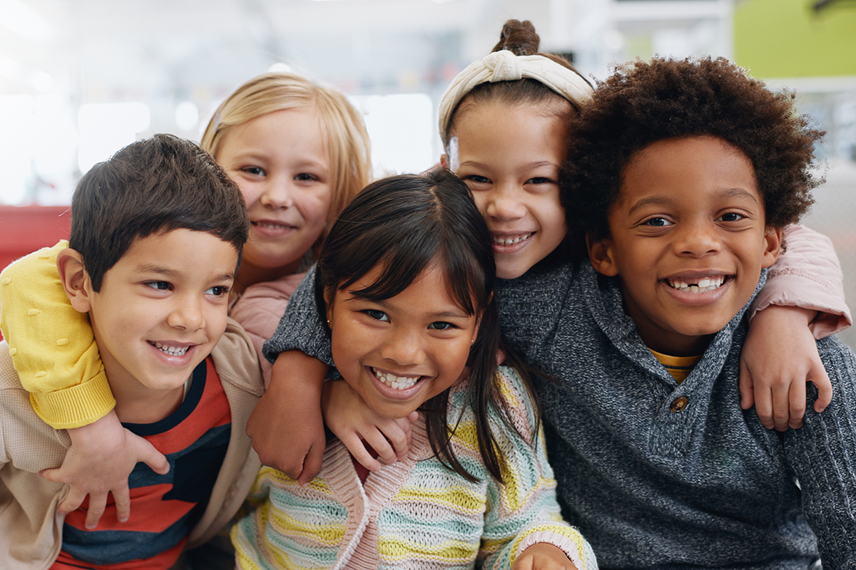 Retrato de um grupo de crianças sorrindo e se abraçando enquanto posam para uma fotografia. 