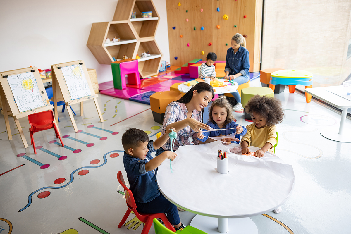 Grupo alegre de crianças se divertindo brincando com slime na escola com a supervisão do professor.