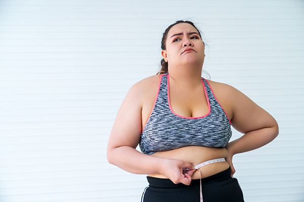 Uma rapariga com excesso de peso mede a sua cintura em frustração devido à memória epigenética. 