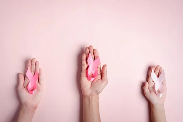 Mãos de mulheres segurando fitas cor-de-rosa sobre um fundo cor-de-rosa.
