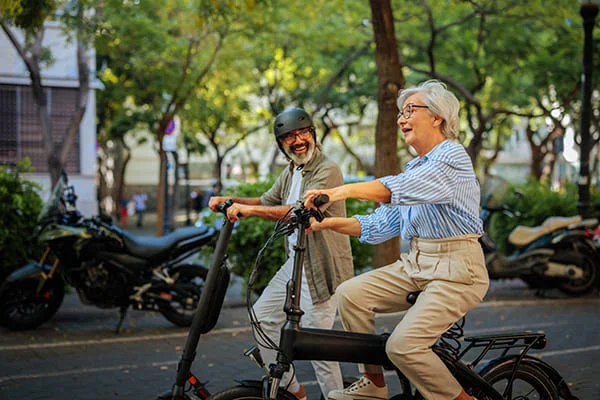 Dois adultos mais velhos a andar alegremente numa bicicleta eléctrica na cidade.