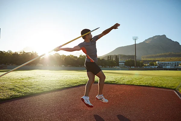 Um atleta praticando lançamento de dardo para moldar a densidade mineral óssea do seu antebraço. 