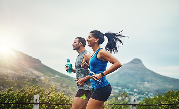 Un hombre y una mujer corriendo, cada uno lleva una botella de agua en su mano para rehidratarse después del ejercicio. Un hombre y una mujer corriendo, cada uno lleva una botella de agua en su mano para rehidratarse después del ejercicio.