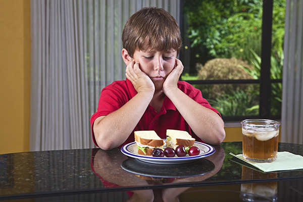 Un niño sentado frente a un plato de comida, pero sin ganas de comer (ARFID). Un niño sentado frente a un plato de comida, pero sin ganas de comer (ARFID).