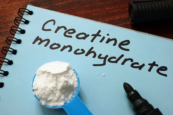 Un cuaderno en blanco con la palabra "monohidrato de creatina" escrita en él, acompañado de una cuchara de creatina. Un cuaderno en blanco con la palabra "monohidrato de creatina" escrita en él, acompañado de una cuchara de creatina.