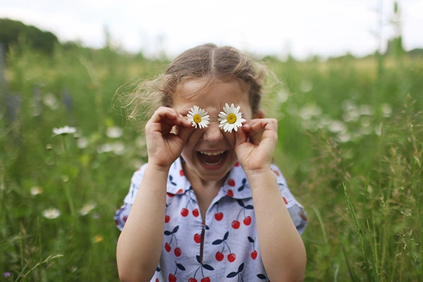 niña jugando al aire libre con unas flores en los ojos.