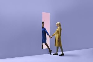 Two women holding hands, walking threw rectangular opening in coloured wall