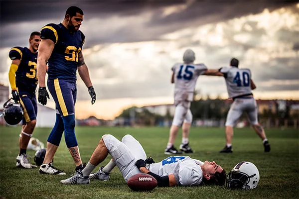 Jugador de fútbol americano tirado en el campo de juego, rodeado de otros jugadores. Jugador de fútbol americano tirado en el campo de juego, rodeado de otros jugadores.